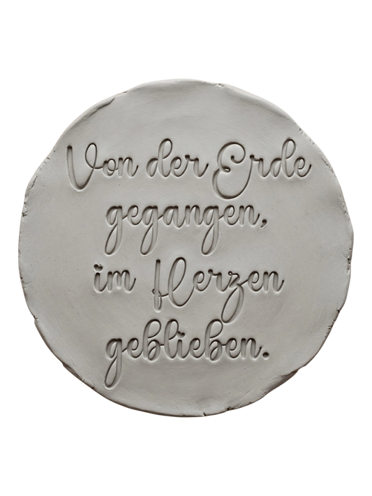 Präziser Stempelabdruck des Textstempels 'Von der Erde gegangen, im Herzen geblieben' in hellem Ton. Das detailreiche Relief zeigt die wunderschöne Schrift perfekt auf einer unglasierten, runden Tonplatte.