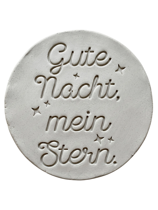 Sauberer Stempelabdruck des Textstempels in hellem, unglasiertem Ton. Die elegante Kombination aus Schrift und kleinen Sternen kommt auf der runden Tonplatte wunderschön zur Geltung.