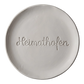 Sauberer Stempelabdruck des Textstempels 'Heimathafen' in hellem, unglasiertem Ton. Die fließende, zusammenhängende Schreibschrift kommt als tiefes Relief auf der runden Tonplatte perfekt zur Geltung.