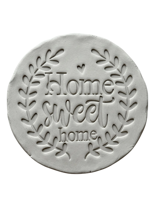 Sauberer Stempelabdruck des Prägestempels 'Home sweet home' in hellem Ton. Das detailreiche Relief zeigt den schönen Blätterkranz und den Schriftzug perfekt auf einer unglasierten, runden Tonplatte.