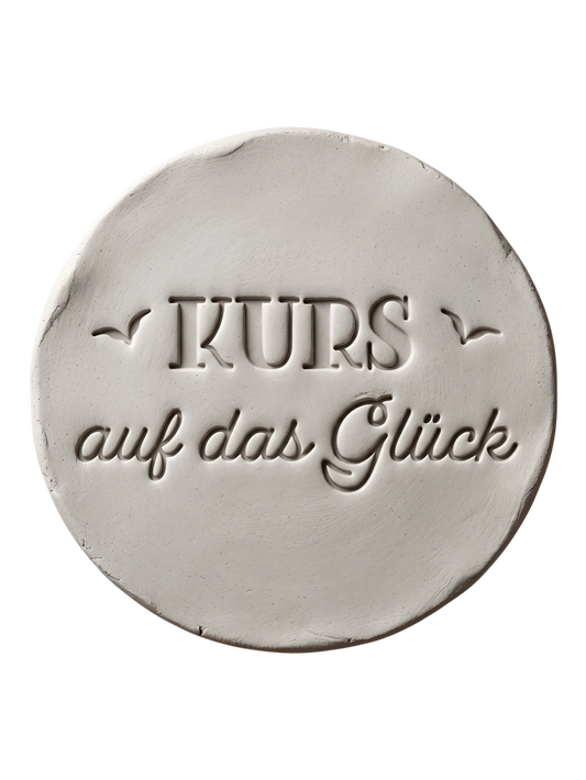 Sauberer Stempelabdruck des Textstempels 'KURS auf das Glück' in hellem, unglasiertem Ton. Die Kombination aus Druck- und Schreibschrift sowie den Vögeln kommt als tiefes Relief perfekt zur Geltung.