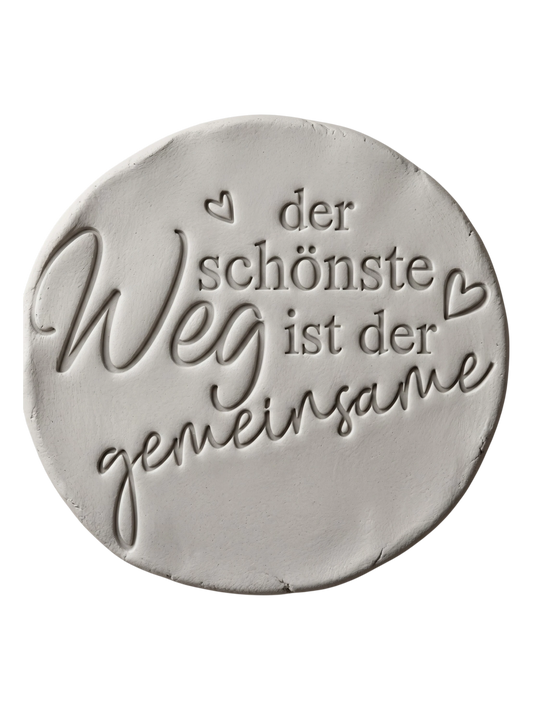 Sauberer Stempelabdruck des Textstempels in hellem Ton. Das detailreiche Relief zeigt den Spruch 'der schönste Weg ist der gemeinsame' mit kleinen Herzen auf einer unglasierten, runden Tonplatte.