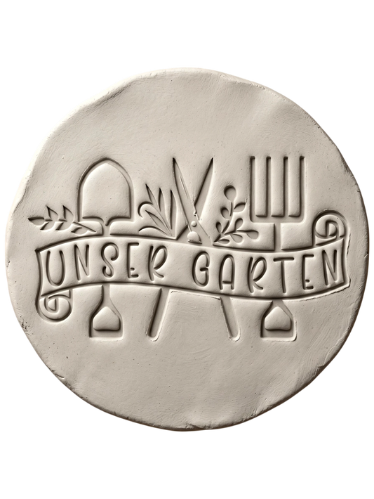 Präziser Stempelabdruck in hellem Ton mit dem Textstempel 'Unser Garten'. Das detailreiche Relief zeigt Gartengeräte und Pflanzenmotive auf einer handgemachten, runden Keramikplatte.